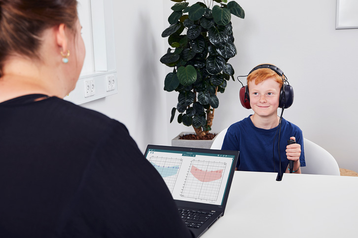 Clinician performing hearing screening in a child wearing headphones and pressing a patient response switch.