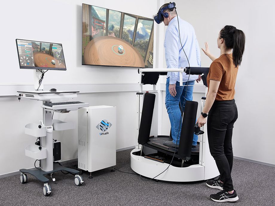 Person in blue shirt doing a training exercise in the MotionVR dynamic posturography platform, with a physical therapist stood behind ready to offer physical support